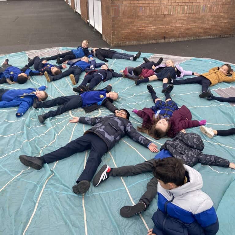 A group of children lying on top of a large blue parachute.